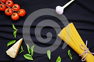 Food frame. Pasta ingredients. Cherry-tomatoes, spaghetti pasta, garlic, basil, parmesan and spices on dark background, copy