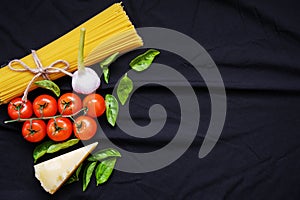 Food frame. Pasta ingredients. Cherry-tomatoes, spaghetti pasta, garlic, basil, parmesan and spices on dark background, copy