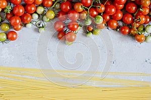 Food frame. Pasta ingredients concept. Uncooked spaghetti and cherry tomato on a blue background. Top view with copy space.
