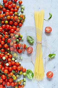 Food frame. Pasta ingredients concept. Uncooked spaghetti and cherry tomato with green basil on a blue background. Top view