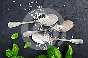 Food frame. Table silver vintage spoons, coarse sea salt, fresh basil on a dark background. Top view. A healthy balanced