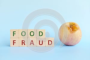 Food fraud concept. Rotten apple beside wooden blocks typography.