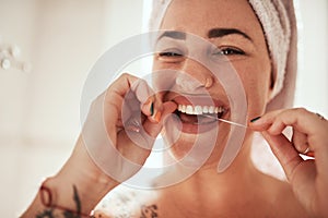 Because food has no place in between your gums. an attractive young woman flossing her teeth in the bathroom at home.