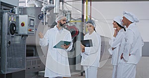 Food industry engineer man holding a tablet in hand and explaining the instructions about the machine to his workers