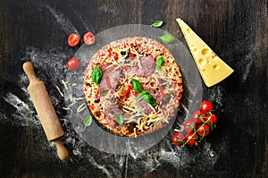 Food ingredients for italian pizza, cherry tomatoes, flour, cheese, basil, rolling pin, spices on dark background. Top