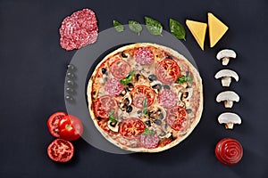 Food ingredients and spices for cooking and delicious italian pizza on black concrete background.