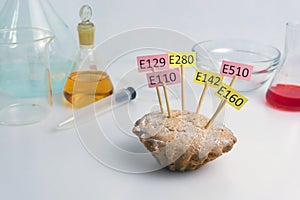 Food laboratory, cupcake decorated with nameplates of additives E, with close-up on a white table.