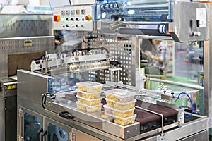 Food in multiple plastic box placed on automatic plastic film wrapping or protective packing machine for goods or other product