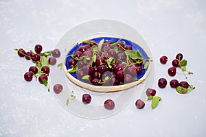 Food photo. Fresh ripe cherries in a plate and on a table on a light background.