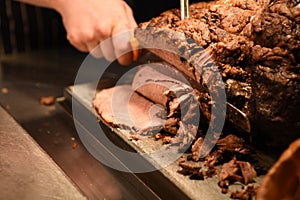 Food photography image of a cooked roast beef joint of meat with hand holding a carving knife and slicing the dinner onto a board