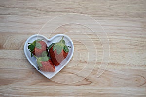 Food photography image of healthy red strawberries in a white love heart shape dish on wood background with copy space