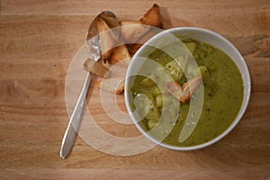 Food photography image of home made broccoli pea potato soup in white bowl with love heart shape toast on rustic wood background