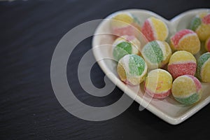 Food photography for Valentines with a white love heart shape dish filled with candy sugar sweets in green yellow and red colors