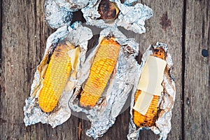 The food at the picnic. Grilled corn and cheese, wrapped in foil. Top view, on a wooden table