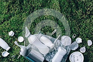 Food plastic packaging, trash on green moss background after picnic in forest. Top view. Copy space. Recycling plastic