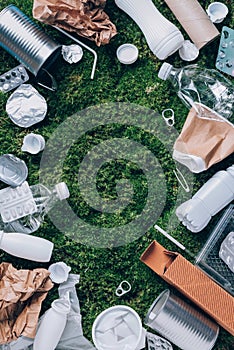 Food plastic packaging, trash on green moss background after picnic in forest. Top view. Copy space. Recycling plastic