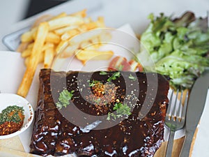 Food pork ribs grilled with BBQ sauce and caramelized in honey with French fries snack on wooden plate