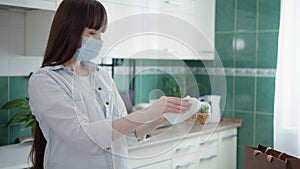 Food processing, adult girl in medical mask observes precautions and disinfects containers with food left by courier at