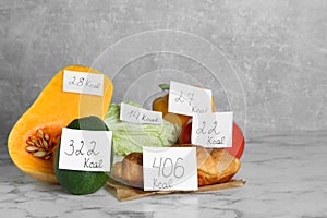 Food products with calorific value tags on white marble table. Weight loss concept photo