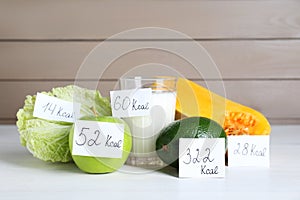 Food products with calorific value tags on white wooden table. Weight loss concept photo