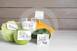 Food products with calorific value tags on white wooden table, space for text. Weight loss concept