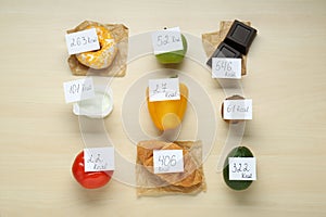 Food products with calorific value tags on wooden table, flat lay. Weight loss concept photo