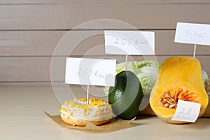 Food products with calorific value tags on wooden table, space for text. Weight loss concept