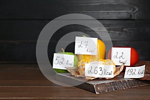 Food products with calorific value tags on wooden table, space for text. Weight loss concept