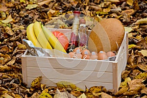 Food set: banana, eggs, nuts, pumkin, coffee, bread, oils in a wooden box against the background of autumn yellow foliage.