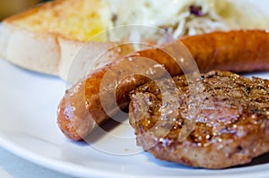 Sausage and pork steak on white dish photo