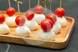 Food snacks and appetizers for buffet. Canapes with mozzarella cheese and cherry tomatoes served on wooden tray