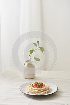 Food, spaghetti bolognese sauce in white dish and a vase of plants on a white prepared table