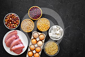 Food for sportsmen. Legumes, nuts, low-fat cheese, meet, eggs on black background top view copy space