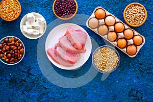 Food for sportsmen. Legumes, nuts, low-fat cheese, meet, eggs on blue background top view space for text