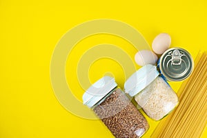 Food stock for quarantine isolation period on yellow background. Rice, egg, canned food, buckwheat, spaghetti. Food delivery,