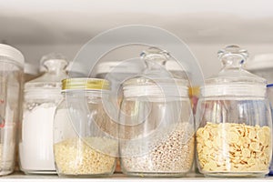 Food stocks on a white kitchen shelf glass jars with cereal, pasta, corn flakes