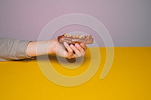 Food in the style of minimalism. Tasty eclair in hand on a gray or yellow background. People lifestyle concept. Mock up copy space