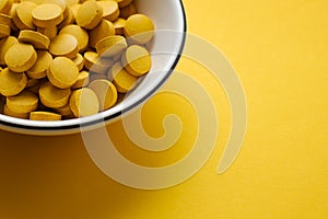Food supplements on white plate,  Yellow pills on yellow background. Dietary supplements with copy space