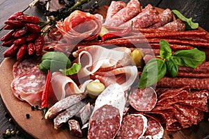 Food tray with delicious salami, pieces of sliced prosciutto crudo, sausage and basil. Meat platter with selection