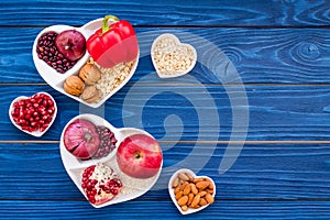 Food which help heart stay healthy. Vegetables, fruits, nuts in heart shaped bowl on blue wooden background top view