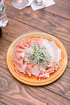 Food wooden plate with delicious salami, pieces of sliced ham, sausage, and greenery. Meat platter with selection