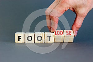 Foot or footloose symbol. Businessman turns wooden cubes and changes word Foot bad to Footloose. Beautiful grey table grey