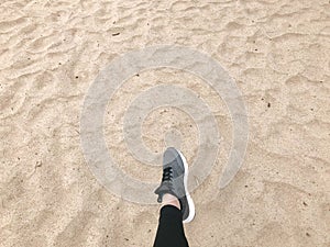 The foot in the gray boot shoe makes a step against the background of a natural loose yellow golden beautiful warm beach sand