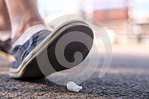 Foot of a man in shoes steps on a lost wireless headphones, which lies on the asphalt sidewalk, outdoors, against a