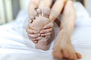 Foot Pain woman sitting on the bed holding her feet at home having painful feet and stretching muscles fatigue To relieve pain.