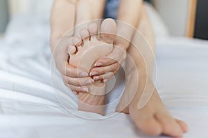 Foot Pain woman sitting on the bed holding her feet at home having painful feet and stretching muscles fatigue To relieve pain.