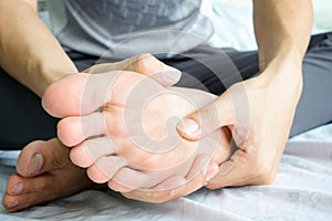 Foot Pain woman sitting on the bed holding her feet at home having painful feet and stretching muscles fatigue To relieve pain.