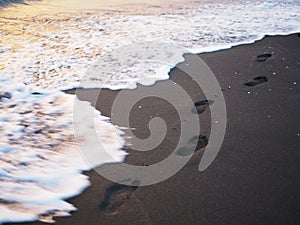 Foot prints on a black sand beach with tilt-shift blur. Surf in background. Concept for loneliness, solitude, depression