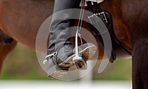 The foot of the rider, sitting on a red horse, in a black boot with a spur, rests on a metal stirrup. Close-up
