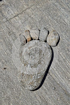 A foot shape with toes made out of rock pebbles sitting on a boulder